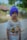 A child is wearing a colorful t-shirt featuring cartoon characters and a purple knit cap. The background shows blurred greenery and a rustic structure, suggesting an outdoor setting.