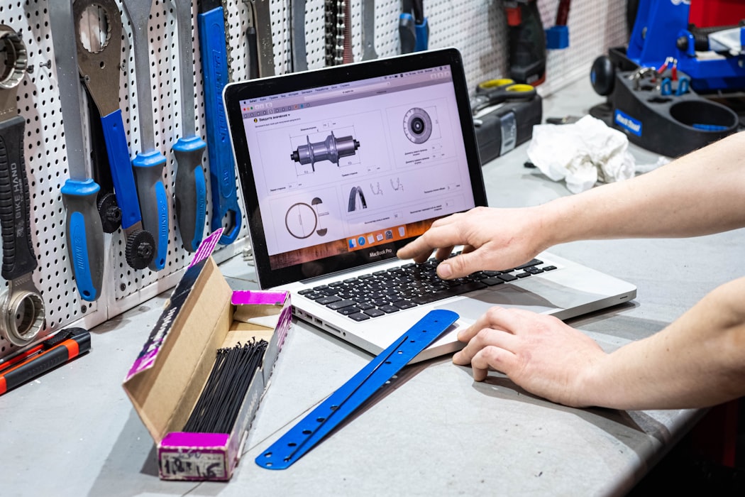 Tradesperson working on a laptop at a shop bench with hand tools on the pegboard behind