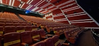 Rows of red velvet seats in a modern cinema hall, softly lit.