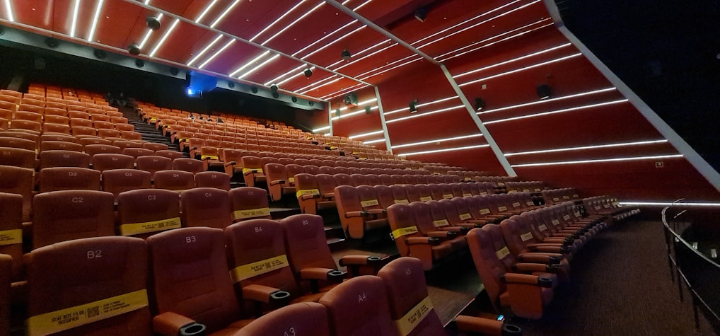 A cozy modern cinema hall with plush red seats and a large screen showing a vibrant movie scene.