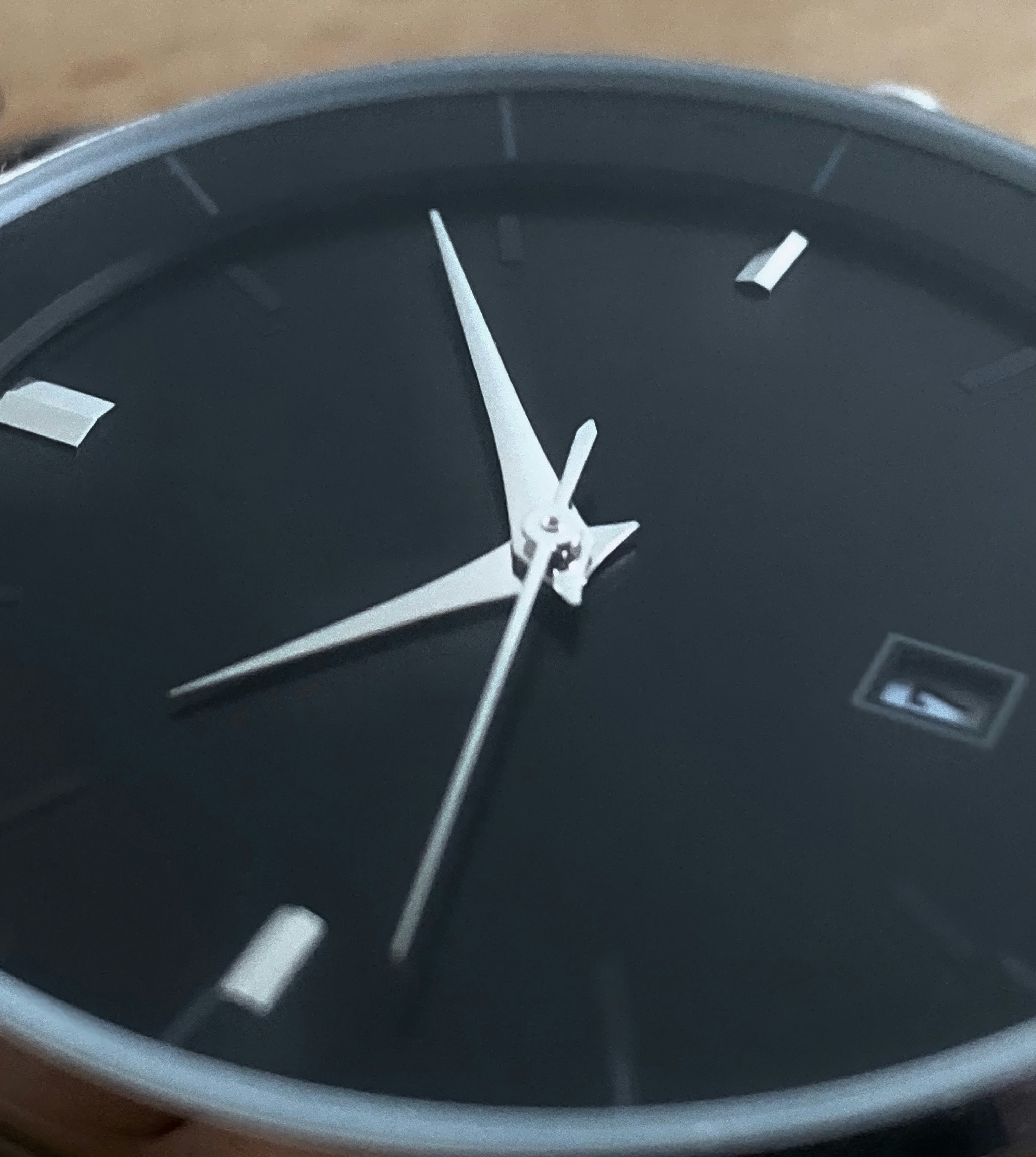 Close-up of a sleek, modern analog watch with a minimalist black dial and silver case.