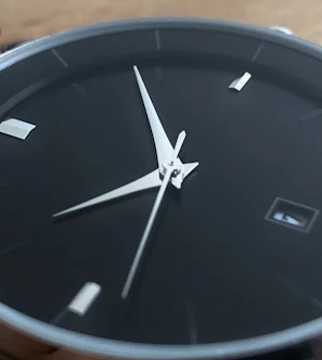 Close-up of a sleek black luxury watch face with silver detailing on a minimalist white background.