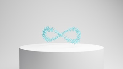 A white cylindrical pedestal displays a floating collection of small, turquoise particles forming the shape of an infinity symbol against a neutral background.