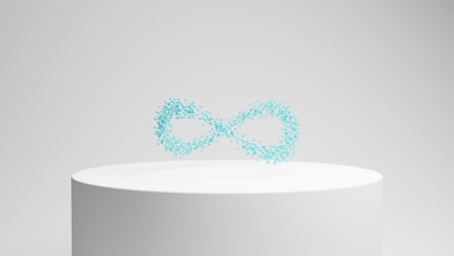 A white cylindrical pedestal displays a floating collection of small, turquoise particles forming the shape of an infinity symbol against a neutral background.