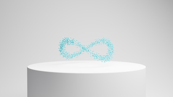 A white cylindrical pedestal displays a floating collection of small, turquoise particles forming the shape of an infinity symbol against a neutral background.