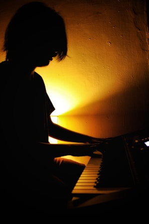 Silhouetted figure behind a glowing keyboard bathed in cool blue and purple hues.