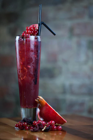 Refreshing frutos rojos pulpa poured into a tall glass with a straw, surrounded by fresh berries and sachets.