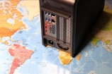 A map of the world overlaid with a computer network device, possibly a server or NAS, is stationed on top, partially covering South America and the Atlantic Ocean.