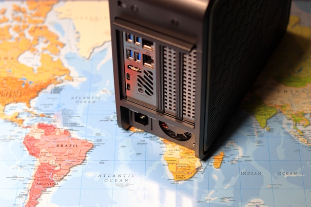 A map of the world overlaid with a computer network device, possibly a server or NAS, is stationed on top, partially covering South America and the Atlantic Ocean.