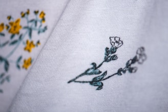 Close-up of fabric with delicate floral embroidery. The fabric is white with embroidered yellow and green flowers on the left side, and green and white flowers on the right side.