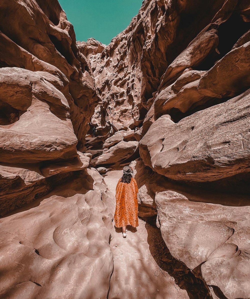 Eine Person in einer orangefarbenen Jacke geht durch einen Canyon