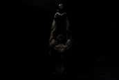 Silhouetted muscular figure lifting weights against a neutral, shadowed background.