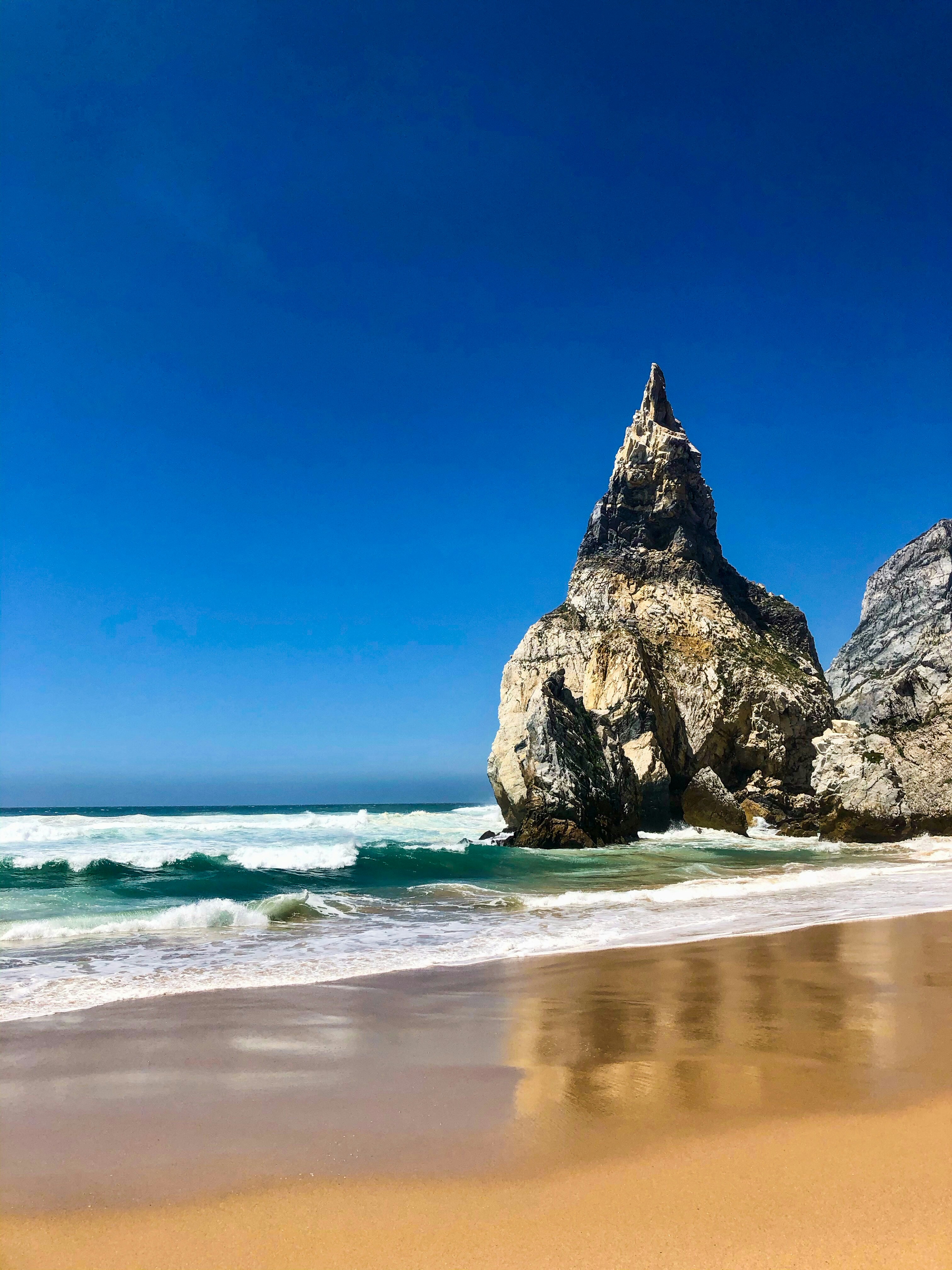 a large rock sticking out of the ocean next to a beach