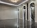 A sleek and modern interior space with polished marble floors and a high ceiling. The room features three tall, arch-shaped panels with decorative lighting and a subtle texture on the walls. A unique ceiling light fixture hangs centrally, adding an elegant touch.