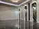 A sleek and modern interior space with polished marble floors and a high ceiling. The room features three tall, arch-shaped panels with decorative lighting and a subtle texture on the walls. A unique ceiling light fixture hangs centrally, adding an elegant touch.