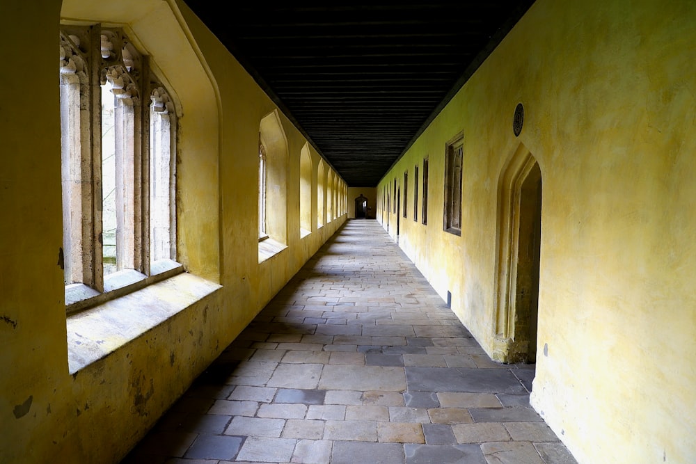 um longo corredor amarelo com janelas arqueadas e piso de pedra