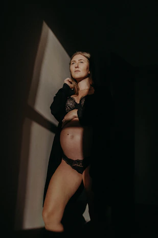 A sensual woman in elegant lingerie posing softly in a dimly lit room.