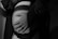 A close-up, black and white image featuring a pregnant belly with two hands gently placed over it, one of which is wearing a ring. The image is intimate and softly lit, highlighting the curves and shadows.