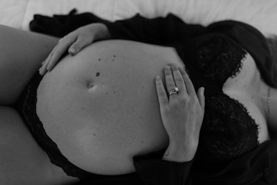 A person wearing a lace bra lies down with hands gently placed on a pregnant belly. The focus is on the peaceful and intimate moment captured in a black and white photograph.