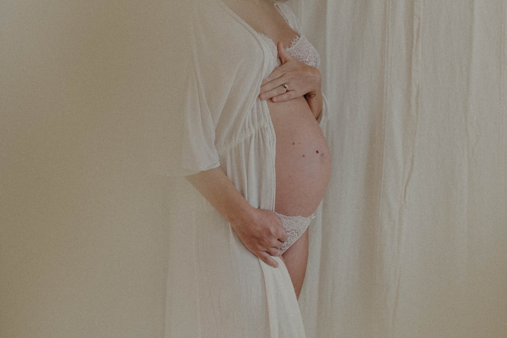 a pregnant woman in a white robe standing in front of a curtain