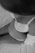 A grayscale image captures a woman with a focus on her pregnant belly. She is wearing a lace bra and a ring, gently cradling her stomach with one hand. A soft fabric drapes over her, adding to the intimate and serene atmosphere.