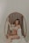 A woman sits in a wicker hanging chair, gently cradling her pregnant belly, wearing a lace bra and a loosely draped white garment. The setting is softly lit, creating a serene and intimate atmosphere.