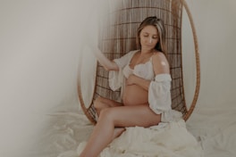 A serene pregnant woman sitting peacefully in a sunlit room, surrounded by soft cushions and plants.