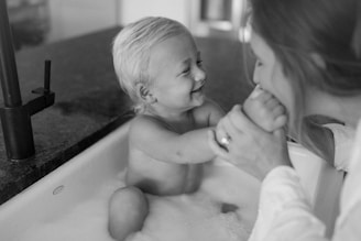 A warm, bright photo of a smiling mother and child brushing their teeth together in a cozy bathroom with turquoise accents.