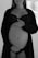A black and white photograph of a pregnant woman. She is dressed in lingerie and a robe, with one hand resting on her upper belly and the other hand positioned below her belly. A ring is visible on one of her fingers. The background is softly blurred, emphasizing her figure.