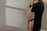 A pregnant woman is dressed in black lingerie, cradling her belly with one hand. The soft lighting creates gentle shadows on the white wall behind her, adding a serene and intimate atmosphere.