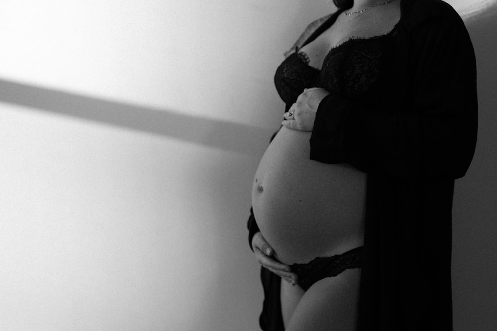 a pregnant woman in lingerie leaning against a wall