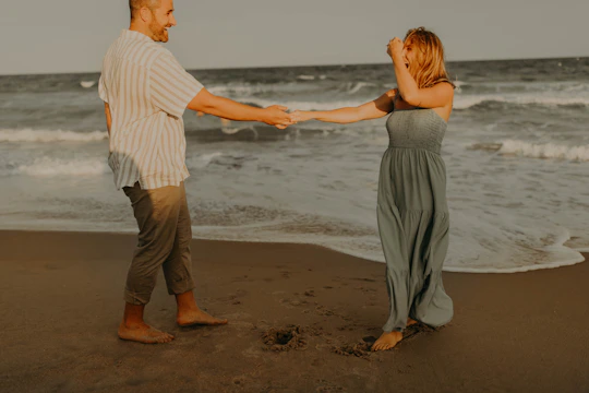 A candid shot of a couple walking hand in hand along a sun-drenched beach, their smiles glowing in the soft sand light.