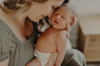 A woman lovingly cradles a newborn baby close to her face. The baby appears peaceful, sleeping in her arms, suggesting a tender and intimate moment. The woman's expression exudes warmth and affection.