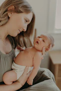 A smiling mother cradling her newborn with a caregiver nearby in a cozy home setting