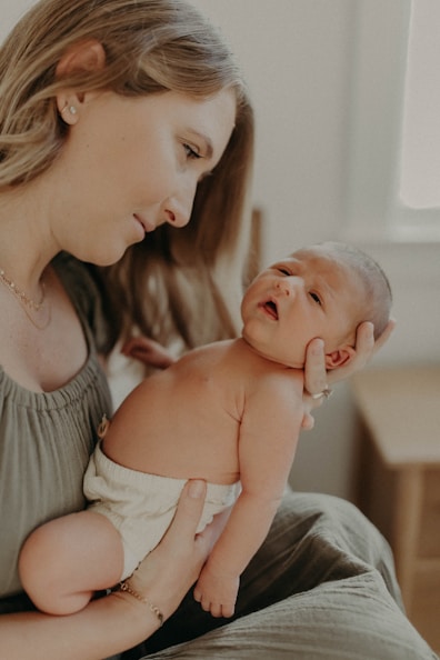A serene mother sitting comfortably in a softly lit nursery, holding her newborn close.