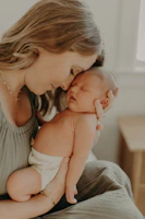A smiling mother holding her baby for the first time, with a doula gently encouraging from beside them.