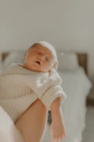 A serene beachside villa where a babysitter gently holds a newborn wrapped in a soft beige blanket.
