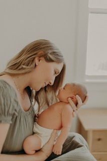A mother holds her baby close, gazing into the infant's eyes with affection. The scene is set in a softly lit room, creating a warm and intimate atmosphere.