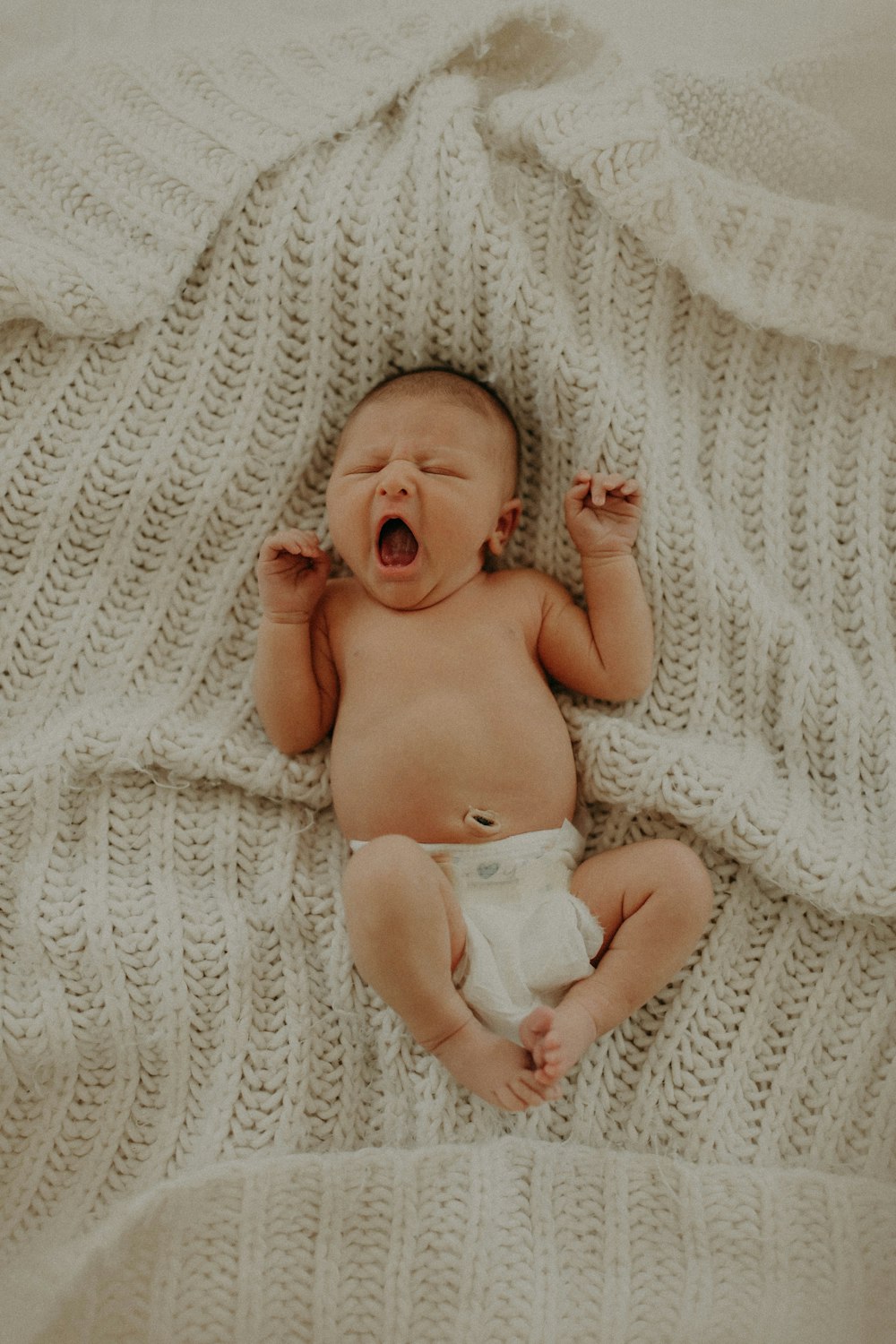 a baby yawns while laying on a blanket