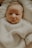 A close-up of a newborn baby wearing a soft, knitted sweater, lying on a light-colored blanket. The baby appears calm and relaxed.