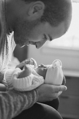 A warm, candid portrait of a newborn baby gently held by their parent in natural light.