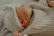 Close-up of a baby sleeping soundly on a light wooden crib covered with a sage green knit blanket.