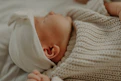 Close-up of a baby sleeping soundly on a light wooden crib covered with a sage green knit blanket.