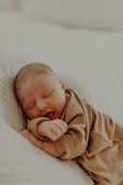 A sleeping baby rests peacefully on a soft surface, dressed in cozy, ribbed fabric. The gentle lighting enhances a serene and tender atmosphere.