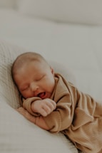 A sleeping baby rests peacefully on a soft surface, dressed in cozy, ribbed fabric. The gentle lighting enhances a serene and tender atmosphere.