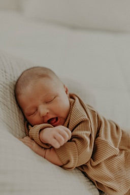 A sleeping baby rests peacefully on a soft surface, dressed in cozy, ribbed fabric. The gentle lighting enhances a serene and tender atmosphere.
