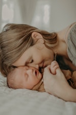 A tender moment between a mother and her sleeping baby, as they gently touch foreheads while the mother holds the baby's hand. The mood is serene and intimate, with soft lighting enhancing the sense of warmth and closeness.