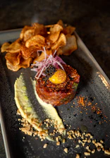 A beautifully plated dish of fresh tartare with vibrant garnishes on a rustic wooden table.
