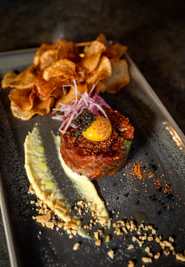 A beautifully plated dish of fresh tartare with vibrant garnishes on a rustic wooden table.