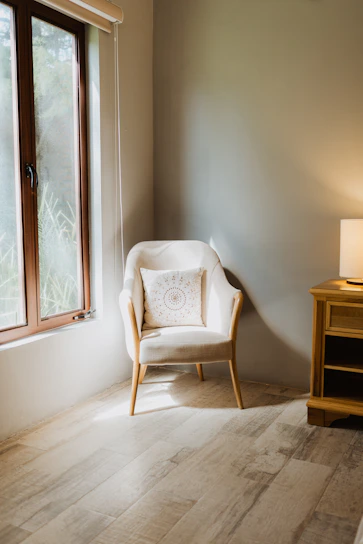 A softly lit living room corner with a chunky knit throw blanket draped over a comfy armchair next to a glowing ambient lamp.